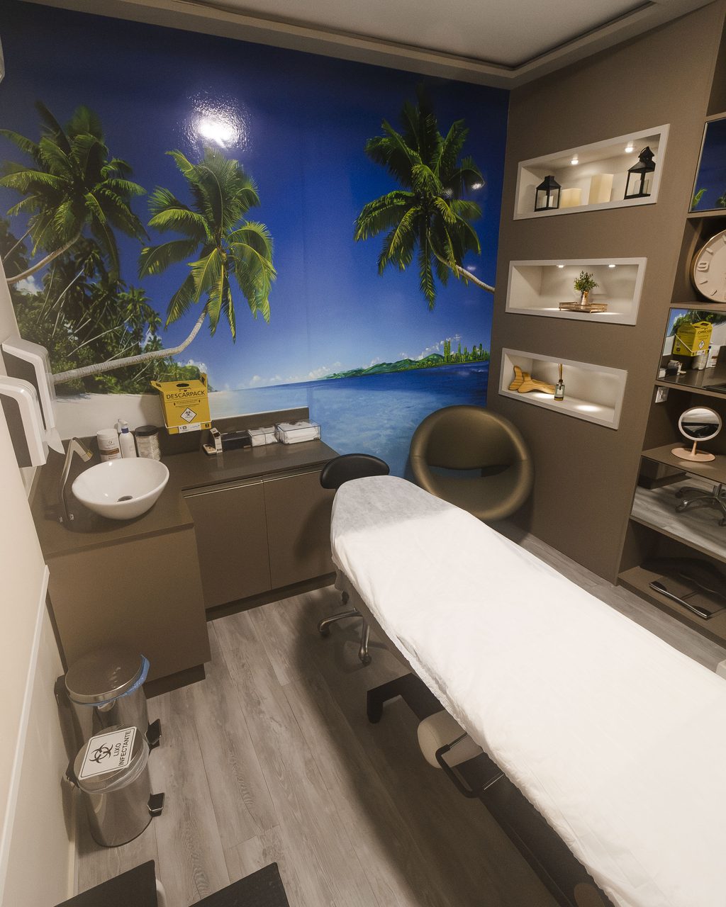 Sala de tratamento da Corpo & Forma com mural de praia, maca preparada e bancada de apoio