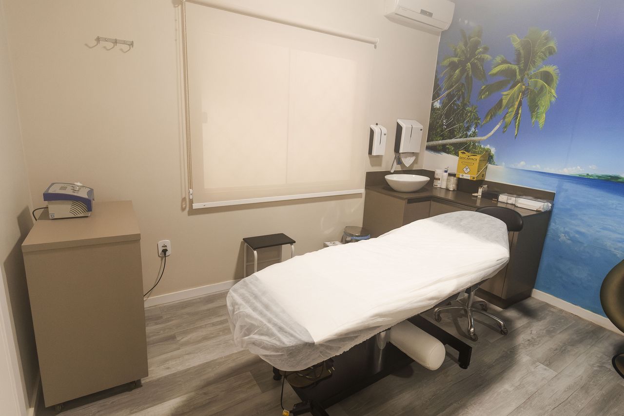 Sala de tratamento da Corpo & Forma com mural de praia, maca preparada e bancada de apoio