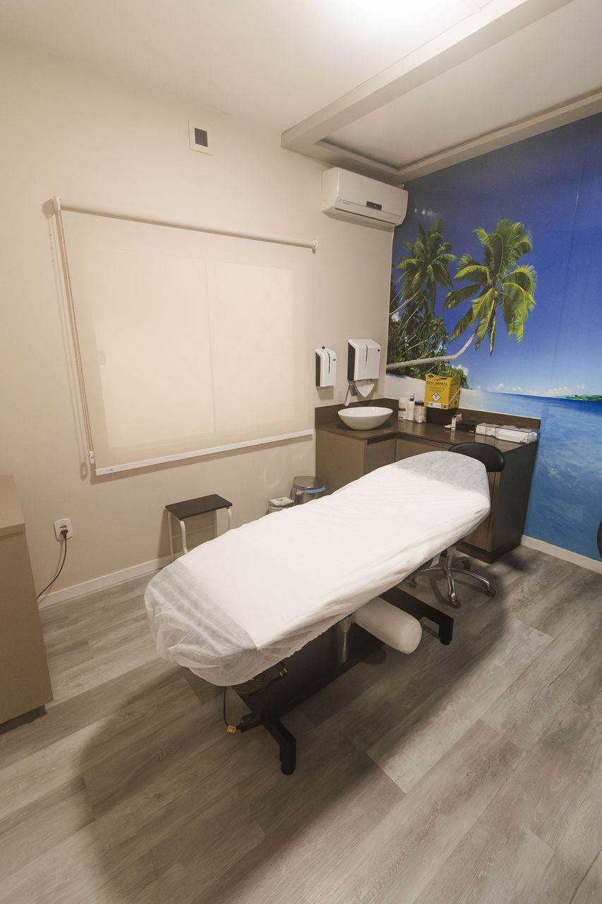 Sala de tratamento da Corpo & Forma com mural de praia, maca preparada e bancada de apoio